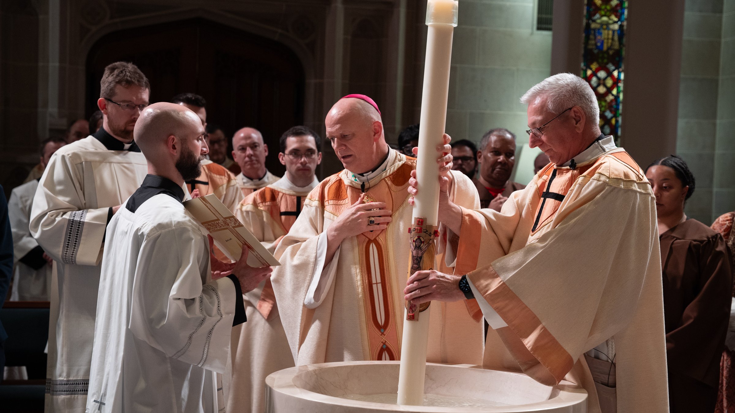 A candlelit Easter Vigil procession inside a historic Catholic church, with congregants holding small candles as a priest leads worship