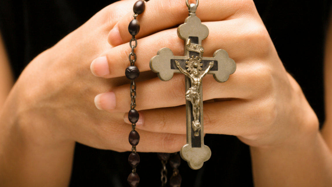 A close view of a person holding prayer beads in their hands while sitting quietly, suggesting a simple repeated prayer practice