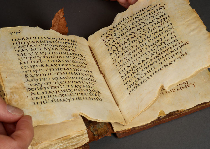 A close view of an old, open Bible or manuscript page displaying text from the Book of Genesis, softly lit on a wooden table