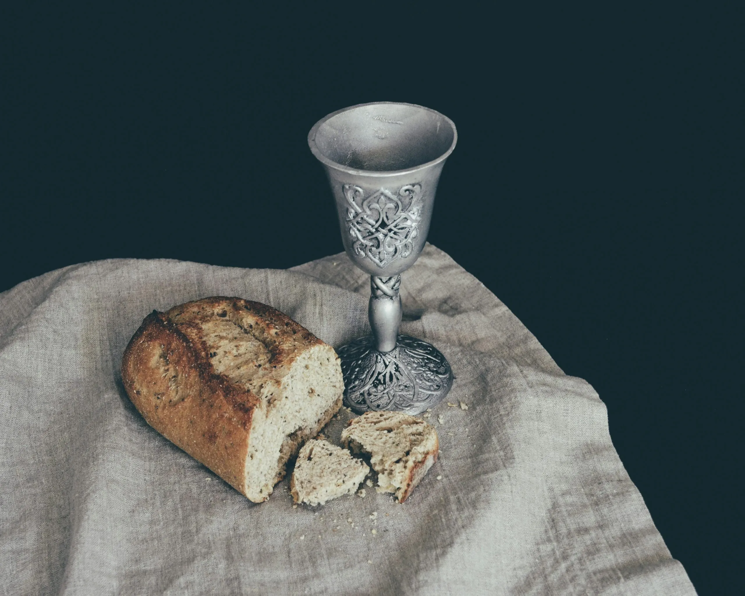 A close view of hands holding a small piece of communion bread near a simple chalice on a church altar, with soft light in the background