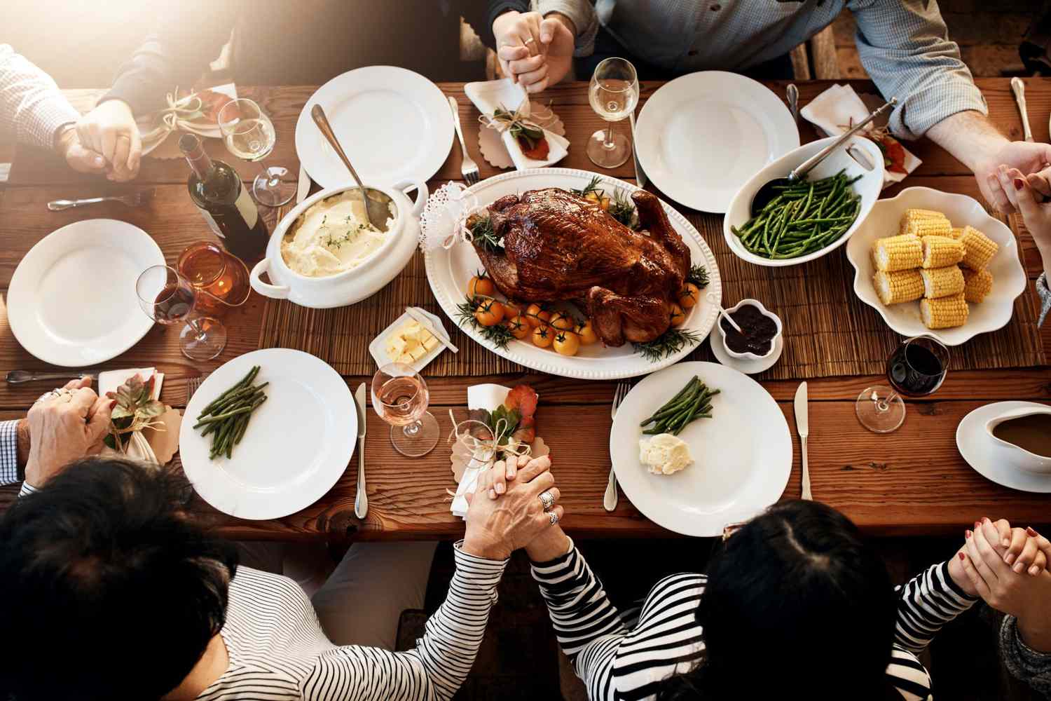 A multigenerational family holding hands and bowing their heads in prayer around a dinner table in a warmly lit home
