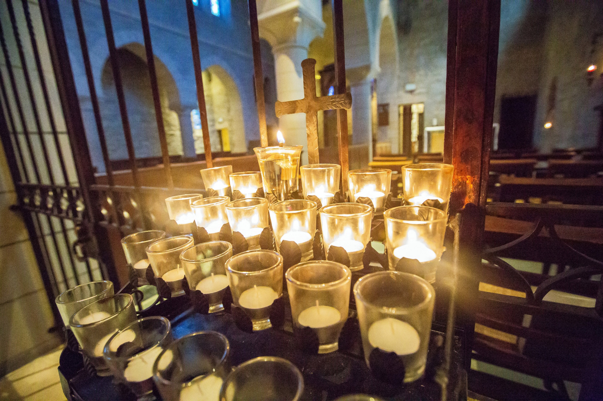 A quiet monastery chapel with a single row of lit votive candles and wooden pews, soft morning light through a small window