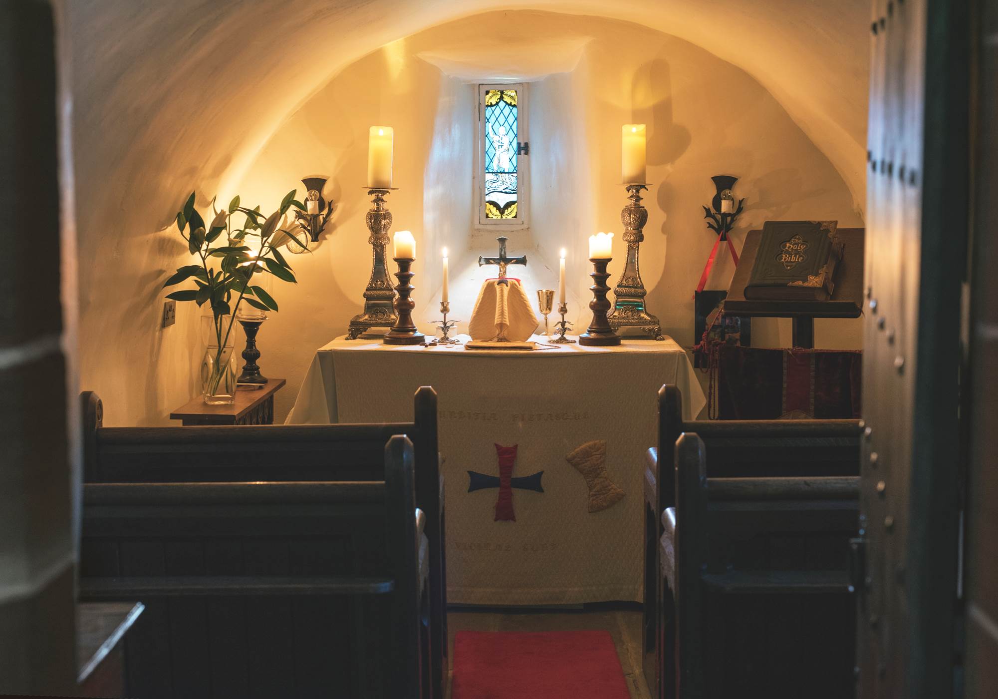 A quiet small chapel interior with a single candle glowing on a wooden table, peaceful and contemplative