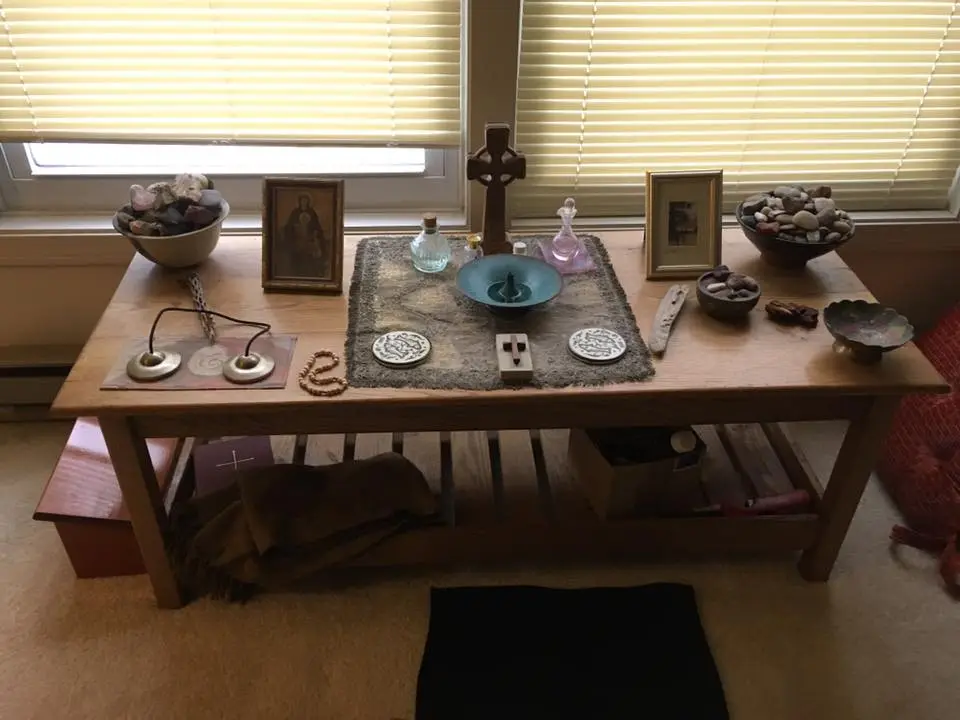 A simple prayer corner with a floor cushion, a small table holding a candle and an open sacred text, and soft natural light