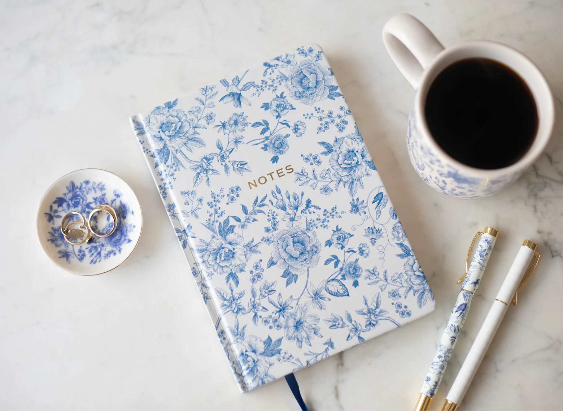 A simple wooden table with a ceramic mug of coffee, an open notebook, and a pen in soft morning light