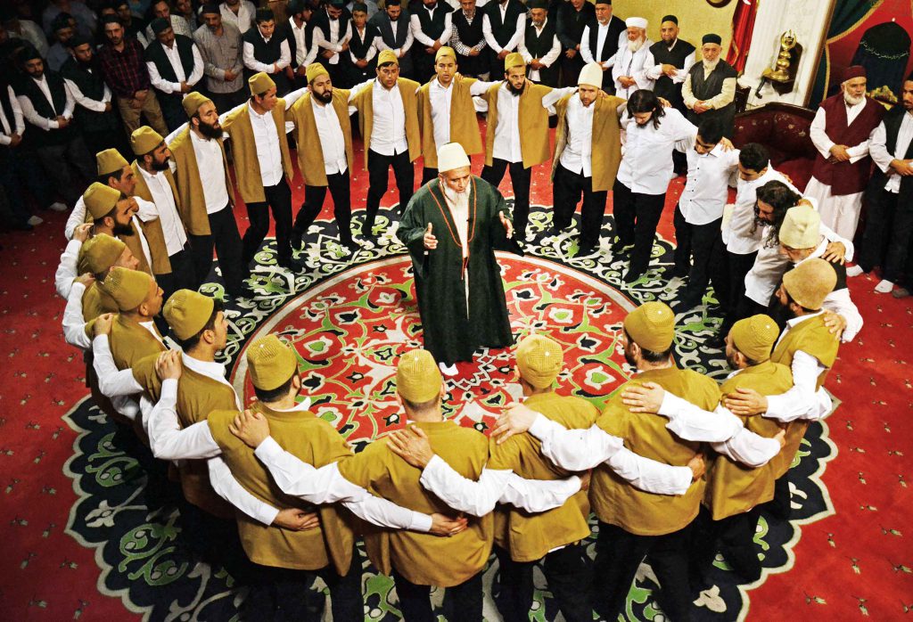 A small group of people seated in a circle indoors during an evening spiritual gathering, hands resting on knees in attentive stillness