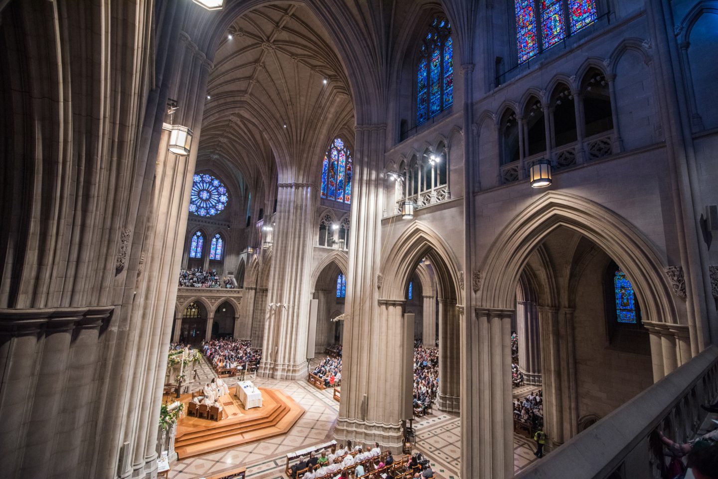 A wide angle view of a welcoming worship space during a service, with people standing and singing while soft light filters through windows