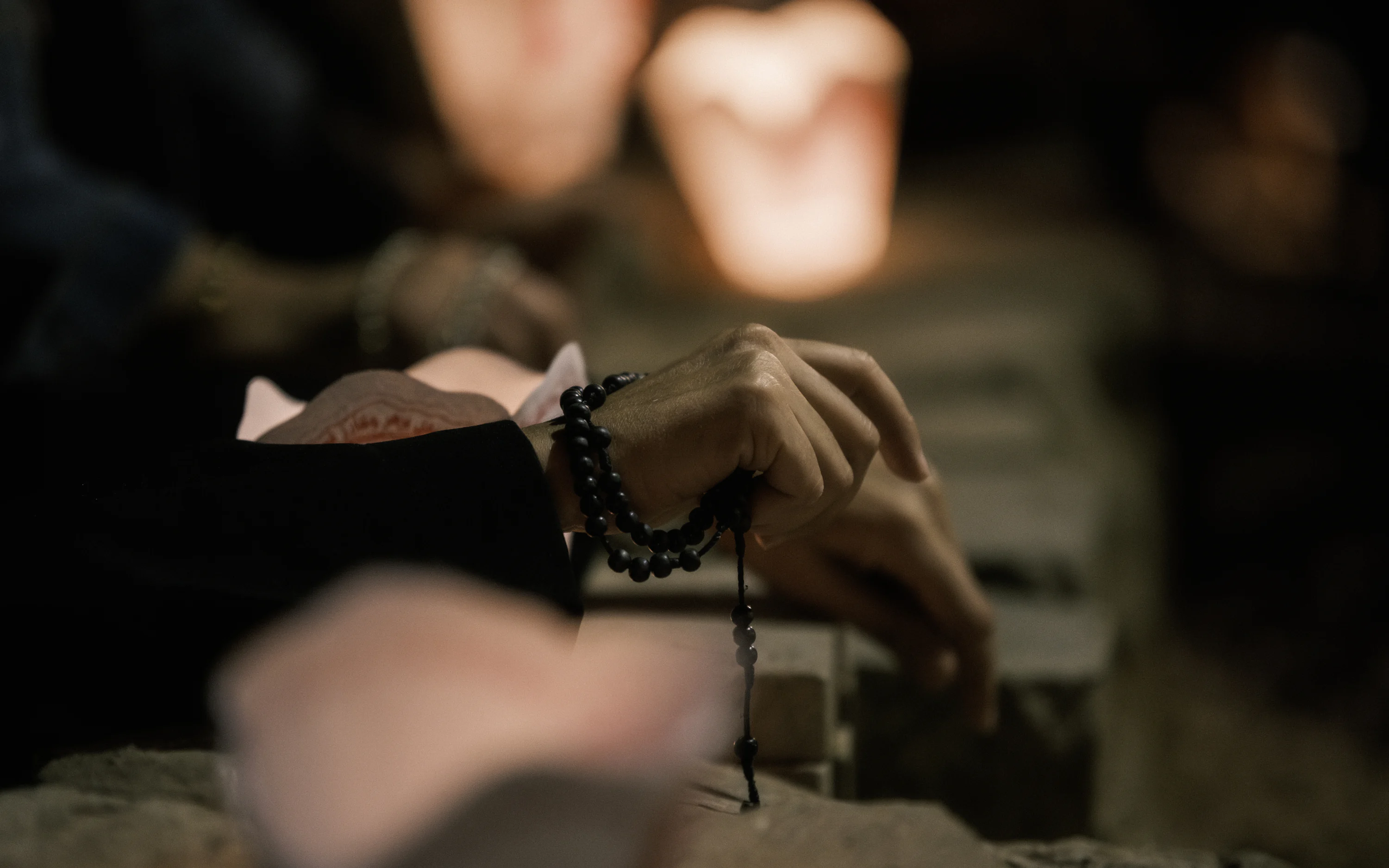 Close-up of a person holding simple wooden prayer beads in their hands, resting in their lap in a quiet room