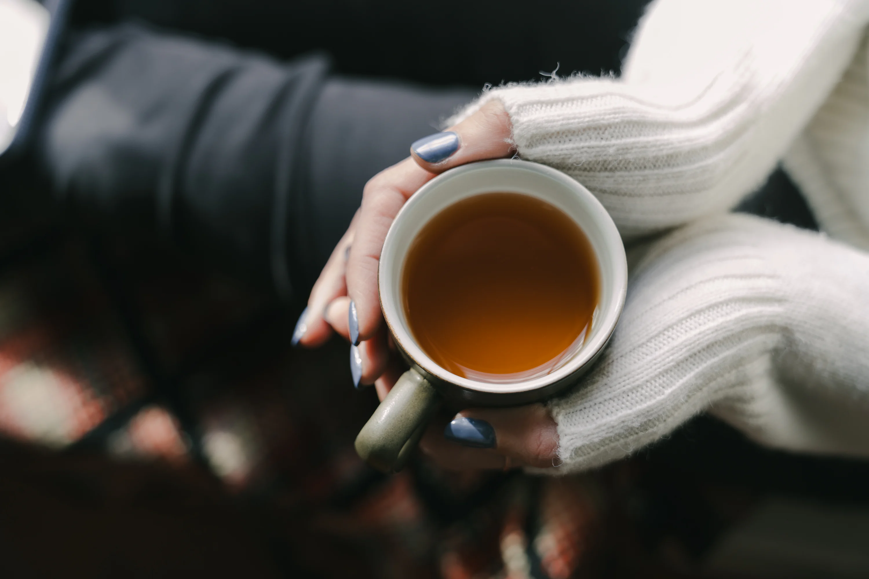 Close-up of hands holding a ceramic mug of tea near a rain-speckled window, suggesting comfort and quiet reflection