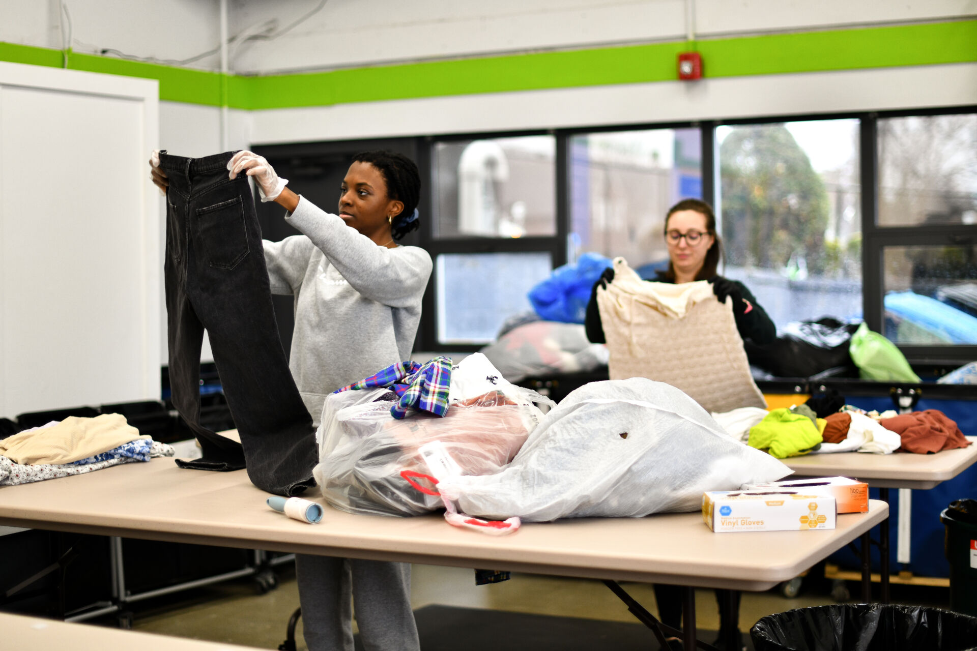 Several volunteers sort donated clothing on folding tables inside a community center while coordinating with each other.